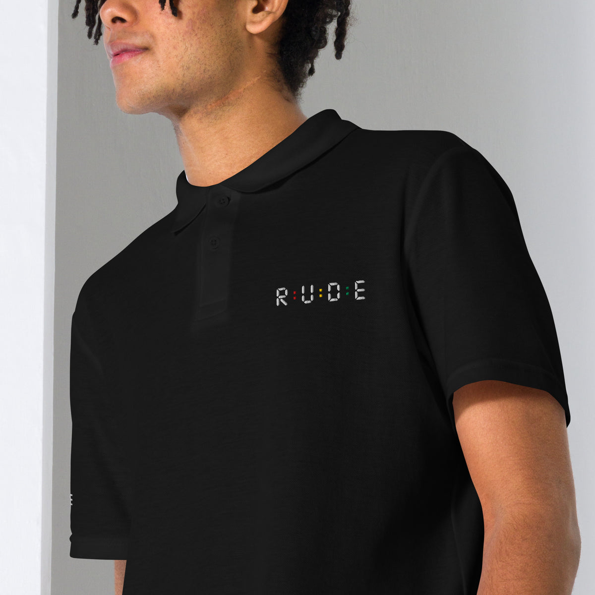 Close-up of black unisex pique polo shirt fabric and embroidered Rude logo